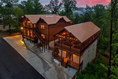 Two multi-level cabin buildings with wraparound decks, ample parking, and mountain tree cover on all sides — a private compound built for the group that goes big on vacation.