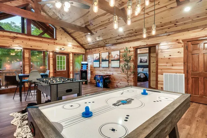 Air hockey, foosball, Edison bulb glow, and vaulted timber overhead — your cabin's game floor is ready for whoever thinks they're the champion this trip.