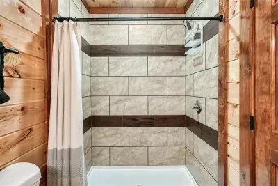 Two-tone tiled tub and shower with warm cabin walls surrounding you — clean, spacious, and built for the group that doesn't want to compromise on bathroom quality.