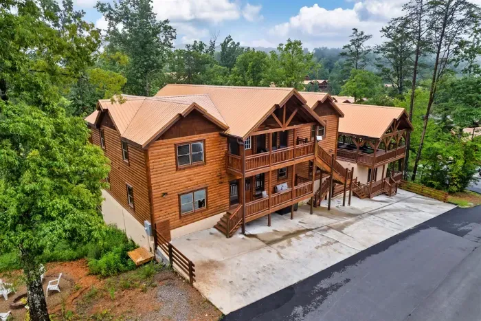 The full picture — a grand multi-level log cabin with soaring timber frames, wraparound decks, and easy driveway access for the whole group. Pull up. You've arrived.