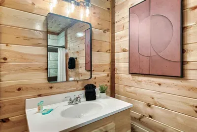 En-suite soaking tub with warm wood walls, oversized mirror, and curated art — a spa-level retreat tucked right inside your private bedroom. You deserve this.