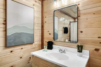 Knotty pine vanity bathroom with a mountain watercolor overhead — the Smokies follow you everywhere in this cabin, even your morning routine. Fresh, bright, and well-appointed.