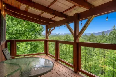 Glass-top table on the covered deck with the ridge line stretching out past the rail. Breakfast outside with a mountain view every single morning.