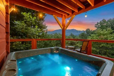 Sunset over the ridge line and the hot tub already bubbling. Covered timber deck, mountain layers rolling out past the rail — the view that ends every day of your stay here.