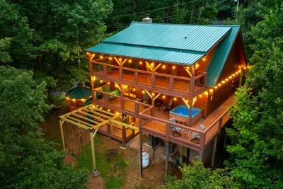 String lights glowing across the decks from above, forest closing in on all sides. The cabin at night looks exactly like the photo you'll post.