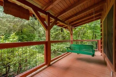 Porch swing under a covered deck with nothing but green past the rail. The most fought-over seat on the property, and worth getting up early for.