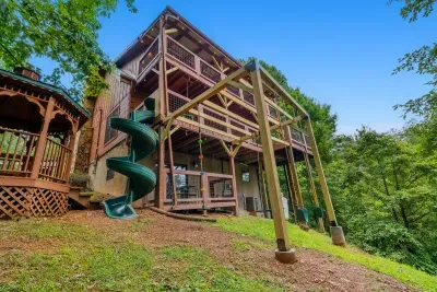 Spiral slide, tiered decks, and the play yard below — the whole property from the side. Built for families who plan to actually be outside.