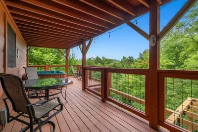 Deck seating with sweeping Smoky Mountain views over the treetops. Layered blue ridges, hardwood canopy, and no other rooftop anywhere in sight.