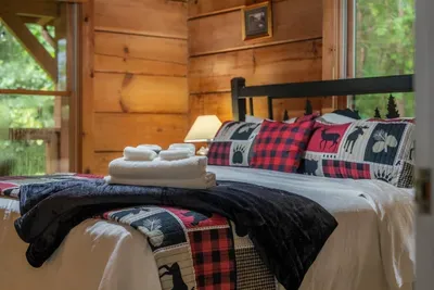 Fresh towels on a bear-print quilt, log walls all around. Made up and ready before you arrive — cabin comfort with the details actually looked after.