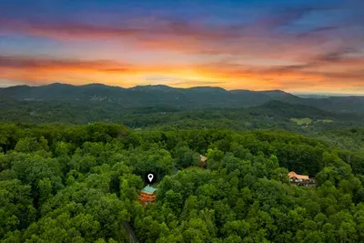 Sunset over the Smokies with the cabin tucked below the ridge. Layered blue mountains, hardwood canopy, and a sky that puts on a show nightly.