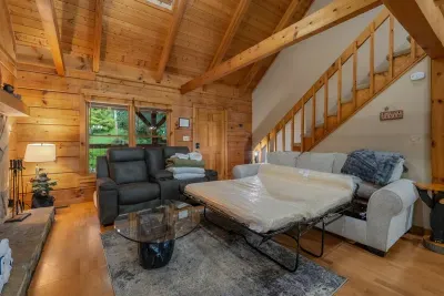 Sleeper sofa and recliner in a bright log-walled sitting room. Extra sleeping space, extra room to spread out, and a window full of green.