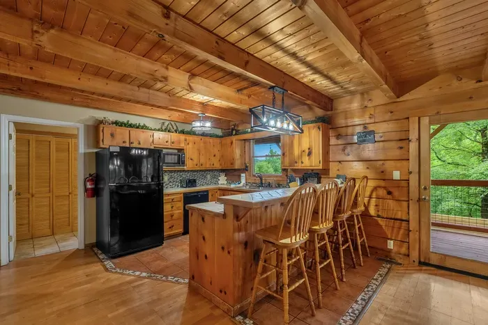 Full kitchen with island bar seating and forest through the window. Cook the group breakfast, pour the coffee, and get out the door toward the mountains early.