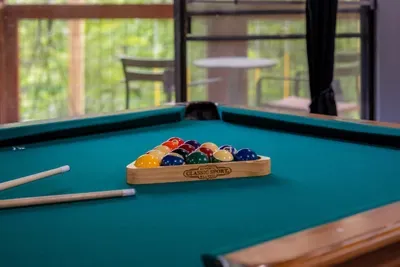 Racked and ready. Full-size pool table with cues on the wall — the break shot that starts the nightly tournament in the lower-level game room.