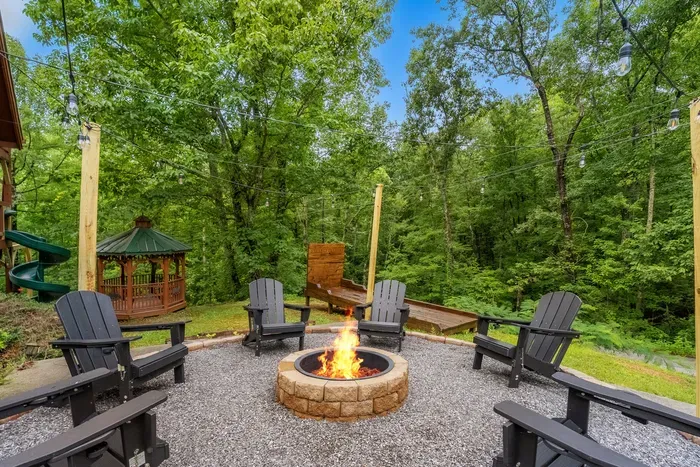 Gas fire pit ringed with Adirondack chairs, gazebo glowing behind and forest on all sides. S'mores at dusk, mountain air, and nobody in sight for miles.