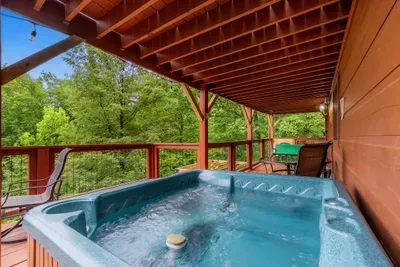 Covered hot tub deck with the forest dropping away below. Soak in any weather — rain on the roof only makes it better up here.