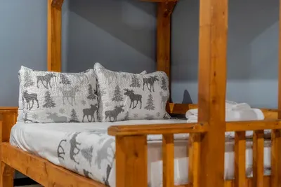 Bunk beds made up with mountain-print bedding and a sturdy ladder. Real mattresses, real linens — the kids' room they'll ask about again next year.