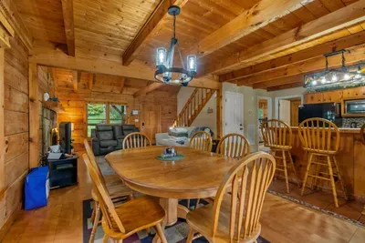 Round dining table under a wrought-iron chandelier, stairs climbing behind. Family-style dinners in a log-walled room — the meals everybody remembers from the trip.