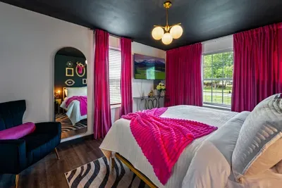 The other side of the most dramatic bedroom in the house — floor-length arched mirror, velvet accent chair, zebra rug, and garden views flooding in through floor-to-ceiling windows.