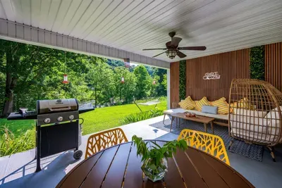 Covered patio with a gas grill, egg chair lounge, ceiling fan, and riverside hammock views — guests call this their favorite spot to "get cozy" and never leave.