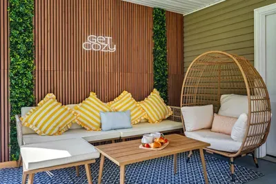 The covered patio lounge that lives up to its neon sign — egg chair, cushioned sectional, wood-slat walls, living greenery, and a snack tray that says someone's already claimed their spot.