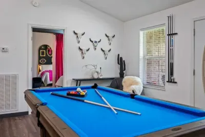 Rack 'em up — the pool table anchors this western-styled game room, complete with longhorn skull mounts, a tucked cue rack, and a peek into the colorful bedroom suite beyond.