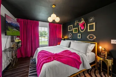 Midnight black walls, hot pink velvet drapes, a gold king frame, and a gallery wall that stops you cold — the most unforgettable bedroom in the house, and guests know it.