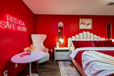 The boldest bedroom in the house — king bed with a sculptural velvet headboard, crimson accent walls, gold mirrors, and a neon sign that sets the whole tone.