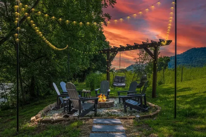 Fire pit, string lights, hanging egg chairs, and a pergola framing that sky — this riverside outdoor lounge is where your evenings will disappear.