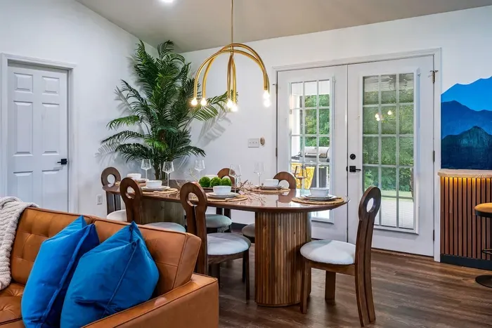 Dining for the whole crew — a sculptural round pedestal table under a gold arc chandelier, French doors to the patio, and that mountain mural keeping watch in the corner.