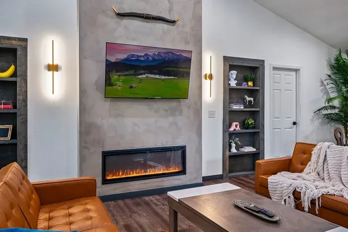 Floor-to-ceiling concrete accent wall, a crackling linear fireplace, gold sconce lighting, and leather sofas draped in chunky knit throws — this is what unwinding actually looks like.
