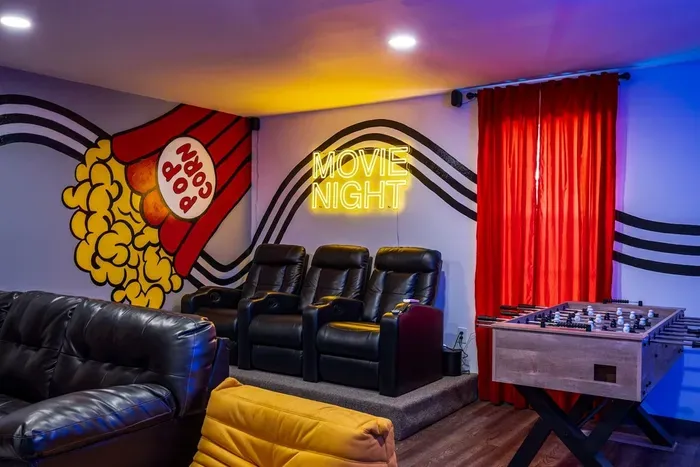 Private theater room with recliner seats, a real popcorn machine, foosball table, and a "Movie Night" neon sign — this is the room that seals the booking every time.