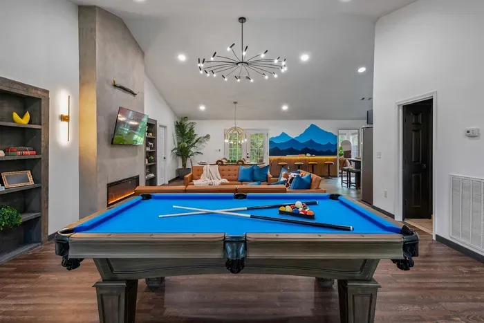Pool table, linear fireplace, wet bar, and a sputnik chandelier anchoring it all — one open-concept great room that handles game night, happy hour, and everything in between.