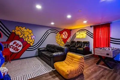 Private theater room with recliner seats, a real popcorn machine, a foosball table, and a "Movie Night" neon sign — this is the room that seals the booking every time.