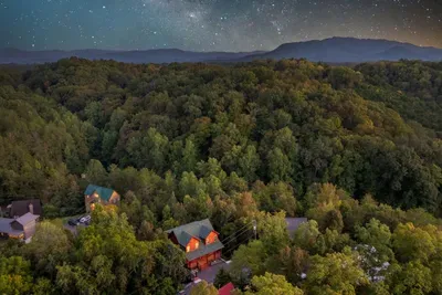 A wider perspective captures the cabin among rolling green hills and distant Smoky Mountain ridges.
