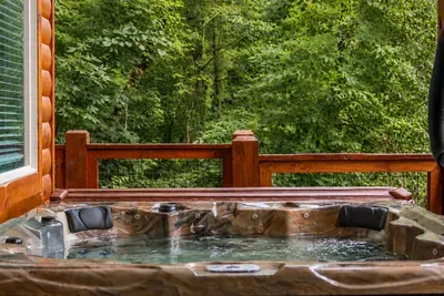 Private hot tub beneath the covered deck, surrounded by the quiet green of the woods.