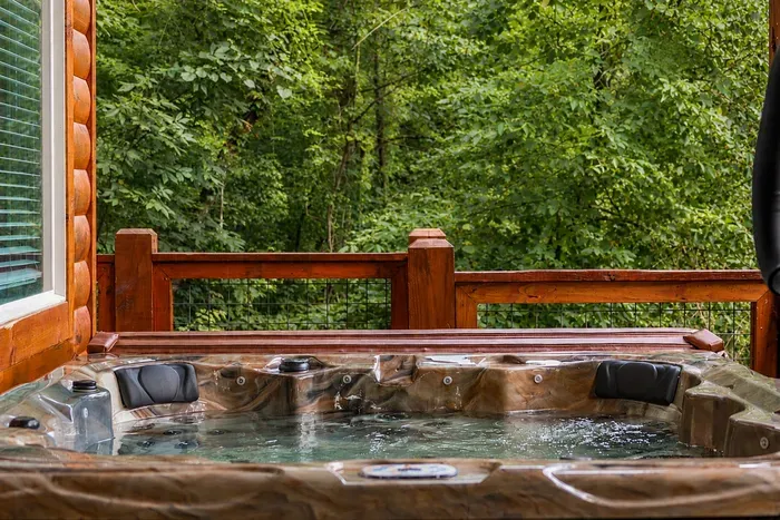 Private hot tub beneath the covered deck, surrounded by the quiet green of the woods.