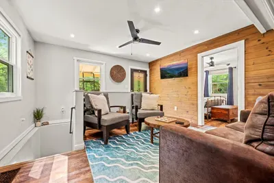 Windows on three sides fill this upstairs living room with light and treetops. Ceiling fan on, feet up, book open — the afternoon takes care of itself.