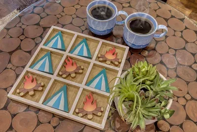 Handcrafted tic-tac-toe on the log-slice table, coffee for two, birdsong for background. The board games are stocked — no Wi-Fi required for the best part of the day.