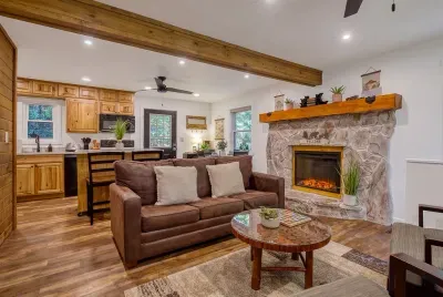 Stone fireplace, reclaimed beam, and a sofa deep enough to disappear into. Open to the kitchen, so the cook never misses the conversation — or the game.