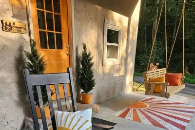 Warm light on the front porch, rockers waiting, swing swaying — the welcome starts before you turn the key. Drop the bags, pour something cold, and let the weekend begin here.