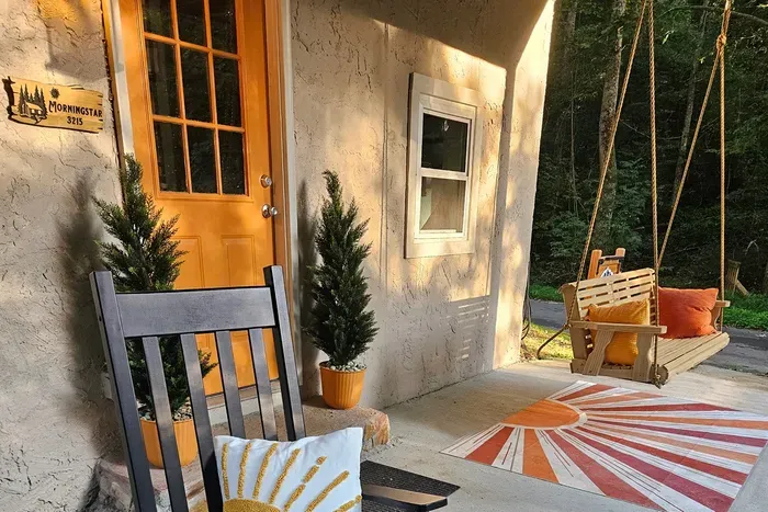Warm light on the front porch, rockers waiting, swing swaying — the welcome starts before you turn the key. Drop the bags, pour something cold, and let the weekend begin here.