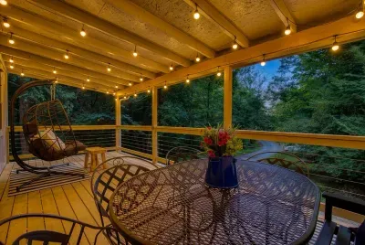 Covered deck strung with lights, cable railings open to the treetops, dinner table set for the group. Rain or shine, this is where the evening ends up.