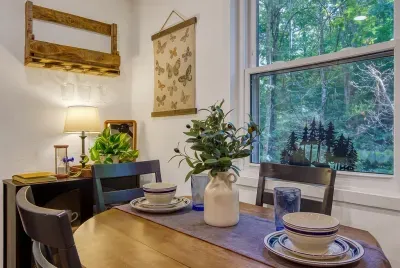 Dining nook set for a slow breakfast, with a window full of forest right beside you. Real dishes, warm light, and a table that fits the whole group for cards after dark.