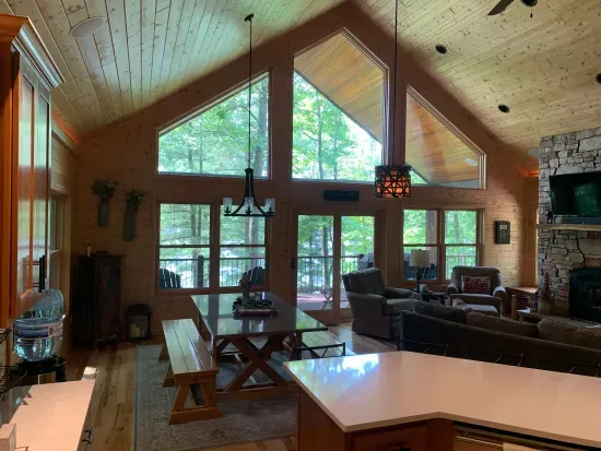 View from full kitchen w/counter-top seating (next to dining table to left) in great room connected to covered deck overlooking lake & above lower level patio & fire pit area.  (Accurate Illustration, AI Enhanced Decor Due to Build In Progress)