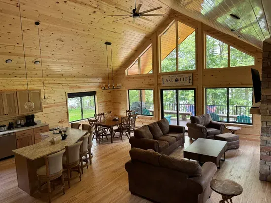 Main level entry view across Lakeside #1 great room, 6-person dining kitchen island, 6-person dining table, family room around gas fireplace, 65" smart TV, access to lake side wrap around deck with BBQ