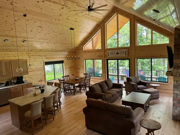 Main level entry view across Lakeside #1 great room, 6-person dining kitchen island, 6-person dining table, family room around gas fireplace, 65" smart TV, access to lake side wrap around deck with BBQ