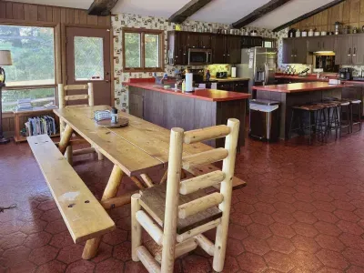 Adjacent to the full eat-in kitchen for four (4) is this view of the rustic pine dining table with log  head-chairs and bench seating for a total of 8-10 dinner guests, depending on how much you like each other!