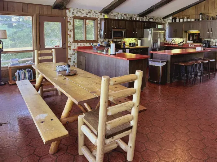 Adjacent to the full eat-in kitchen for four (4) is this view of the rustic pine dining table with log  head-chairs and bench seating for a total of 8-10 dinner guests, depending on how much you like each other! 