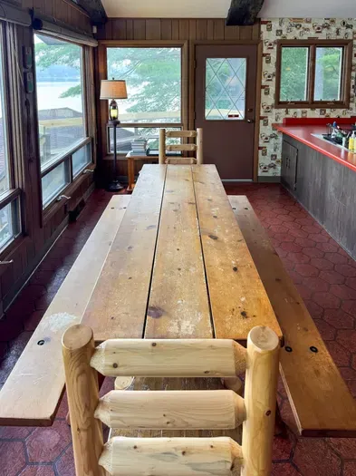 Close up view of the rustic dining table with exit / direct access to the deck overlooking the lake, providing stair access to the lake / boat dock / swimming area below as well as stair access to the expansive BBQ and fire pit area.