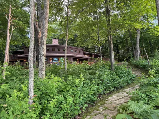 Lakeside view of the Peninsula Lakehouse and the expansive wrap around deck and path leading to private lakes access, boat dock, swimming area, and lake side fire pit.